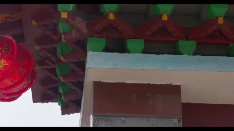 Red lantern swaying in wind under traditional roof, no people Stock Footage 329766846