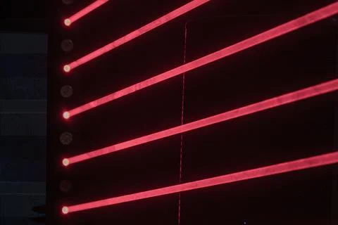 Red laser beams create a dynamic diagonal pattern against a dimly lit interio Stock Photos