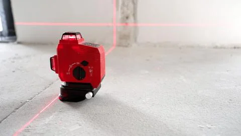 Red laser level emits bright cross lines on gray concrete floor white wall. M Stock Photos