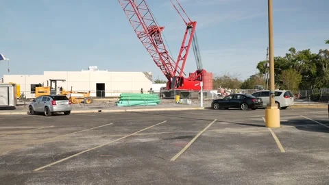 Red lattice boom crane view from parking lot with a palm tree to the left and se Stock Footage 305069840
