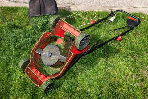 Red lawn mower upside down and container full of grass Stock Photos