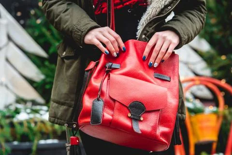 Red leather backpack in hands of a young woman, posing in street of city. Stock Photos