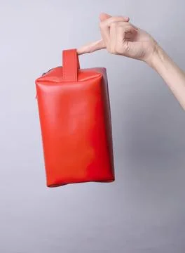 Red leather bag held by hand against gray background Photos