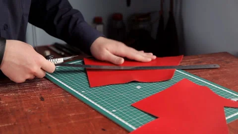 From a red leather layer the man cuts out preparations of skin, using a leather Stock Footage 88873628