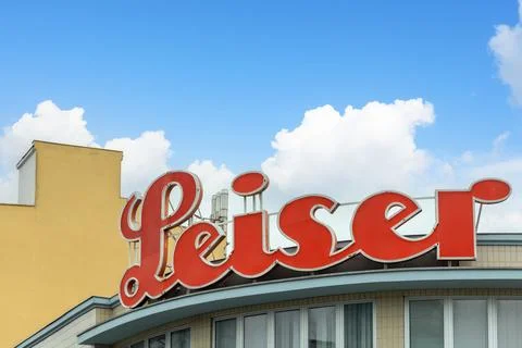 Red "Leiser" cursive signage on a building against a blue sky with clouds. Co Stock Photos