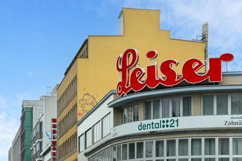 Red "Leiser" cursive signage logo on a building. Urban cityscape with various Stock Photos
