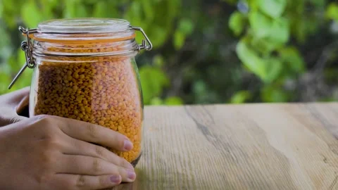 Red lentils jar lifted by hands on wooden table with leaves background, 4K Stock Footage 341424904