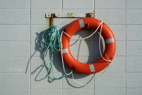 Red life saving ring hanging on a breeze block wall. Stock Photos