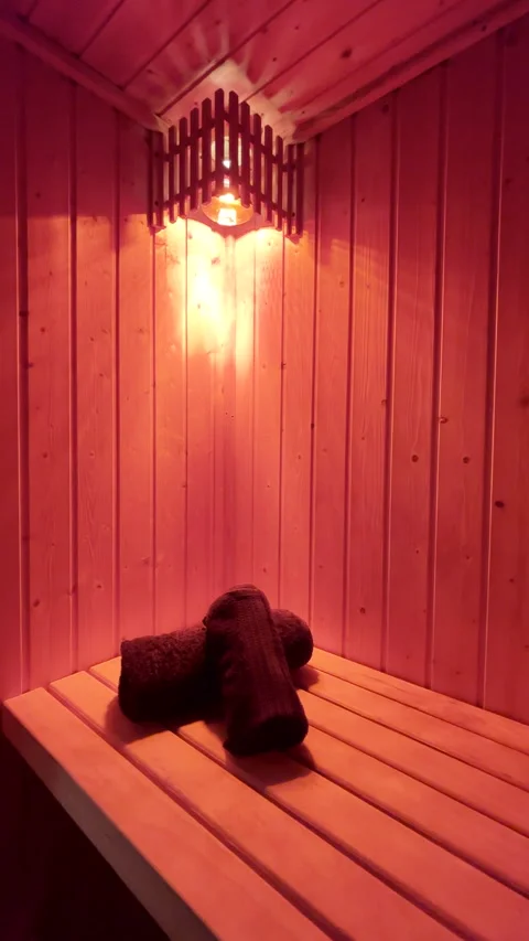Red light above two folded towels illuminates wooden sauna Stock Footage 344010403