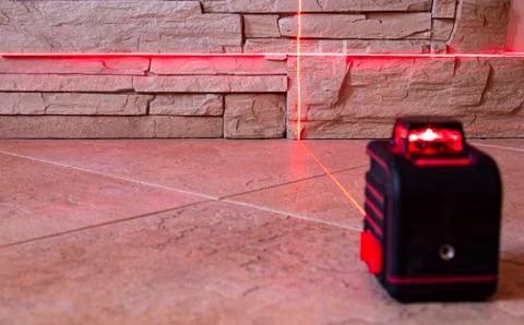 The red light beams of the laser level device on the wall and floor show the Stock Photos