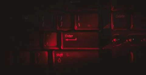 Red light is highlighting on keyboard's enter button in dark . Stock Photos