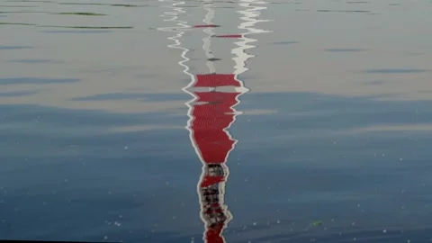 Red lighthouse reflection in rippling water and small stones Stock Footage 136186687