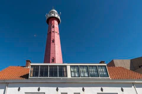 Red lighthouse standing behind a small house against a pur blue sunny and bri 库存照片