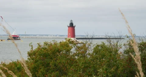 Red lighthouse on water filled bay next to ocean overcast day  Stock Footage 163480225