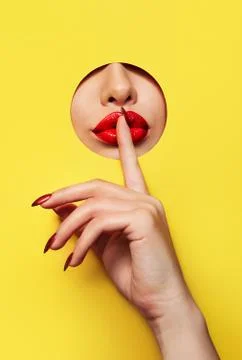Red lips look through the hole in the yellow paper. A finger with a red varnish  Stock Photos