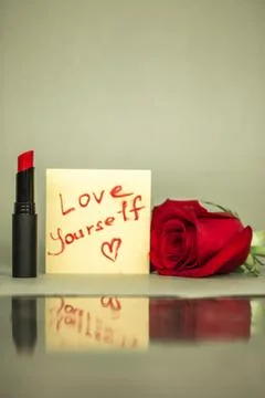 Red lipstick and a note with text Love yourself on cosmetic table, glass mirror Stock Photos