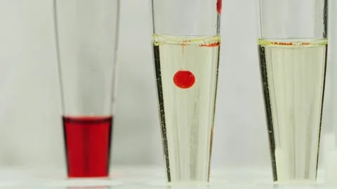 Red liquid drop descends into transparent solution in laboratory test tube .. Video stock 334993201
