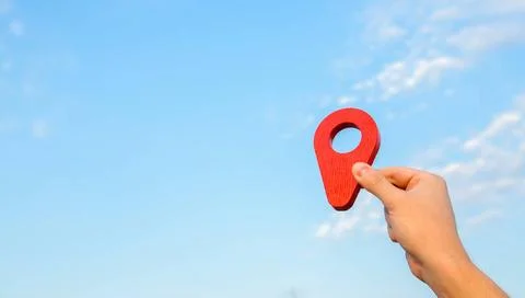 Red location pin in hand on sky background. The concept of location and or... Stock-Fotos