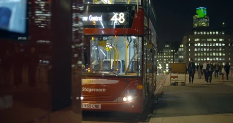 A red London bus pulling away from a bus stop in London at night Stock Footage 87340465