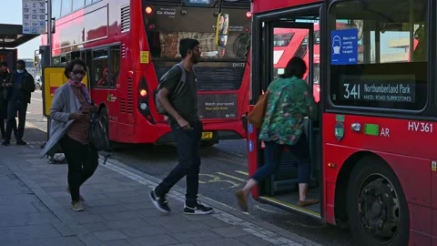 A Red London Double Decker Bus pulls into a bus stop and people get onto the bus Stock Footage 159234902