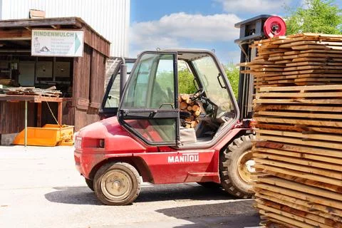 Red Manitou Forklift Parked by Stack of Wooden Lumber at German Sawmill 写真素材