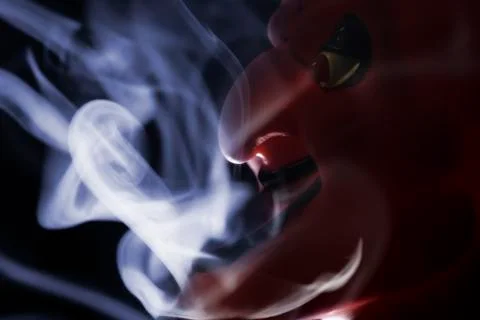 Red mask of devil in smoke on black background. Stock Photos