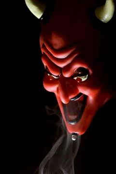 Red mask of devil in smoke on black background. Stock Photos