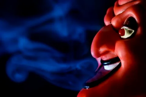 Red mask of devil in smoke on black background. Stock Photos