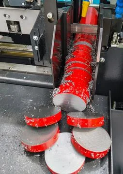 Red metal discs being processed and cut by machinery in a manufacturing facility Stock Photos