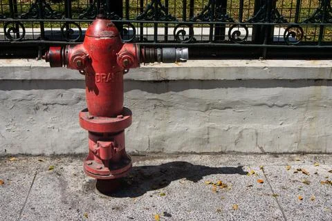 Red metal fire hydrant on sidewalk beside concrete wall and black iron fenc.. Stock Photos