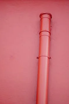 Red metal pipe on solid pink wall, minimal urban detail background Stock Photos