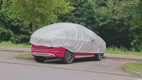 Red modern crossover SUV parked in a lot under a gray protective weather cover Stock Footage 341491654
