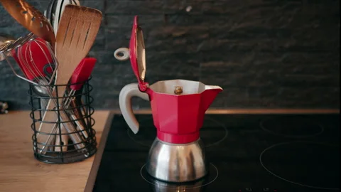 Red moka pot coffee maker placed on a modern kitchen stove next to a container w Видео 331170807