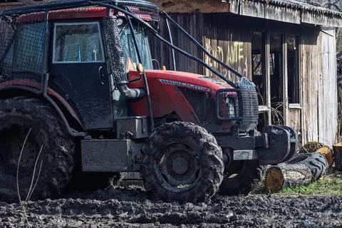 Red Muddy Tractor Parked By Rustic Shed After Logging Work On Rural Farm Pr.. Stock Photos