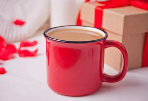 Red mug of coffee, gift box and red rose petals on the gray table 库存照片