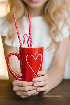 A red mug with a heart pattern with cocoa and paper tubes in the hands of a w Foto stock