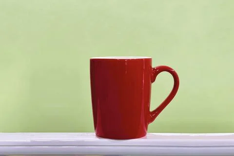 Red mug on the ledge with mild green background. Stock Photos