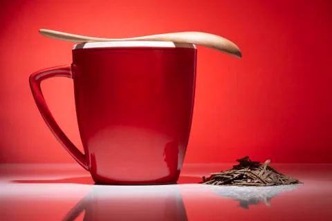 Red mug, small pile of tea and spoon on red background Stock Photos