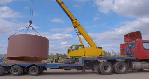 A red multi-axle platform truck arrives for loading, a yellow truck crane lifts  Stock Footage 161963590