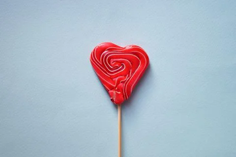 Red multi-colored lollipop in the form of a heart. Blue background. Stock Photos