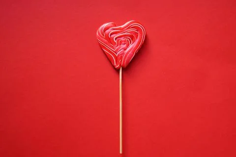 A red multi-colored lollipop in the shape of a heart. On a red background. Stock Photos