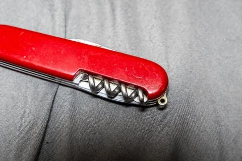A red multi-tool Swiss Army knife on gray fabric background, showcasing its Stock Photos