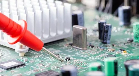 Red multimeter probe measuring a tiny electronic component on a green printed Stock Photos