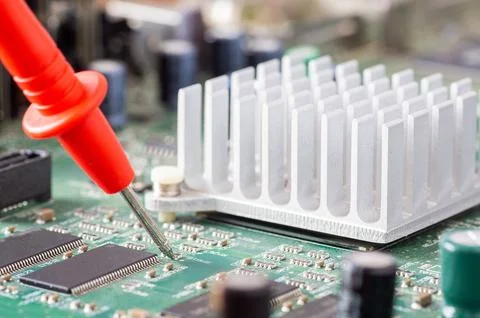 Red multimeter probe testing electronic components on a green circuit board w Stock Photos