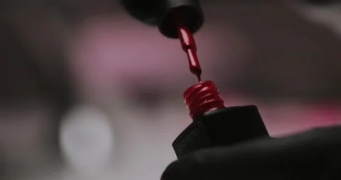Red nail polish with an open bottle and a drop dripping into a jar with a brush Stock Footage 149367348