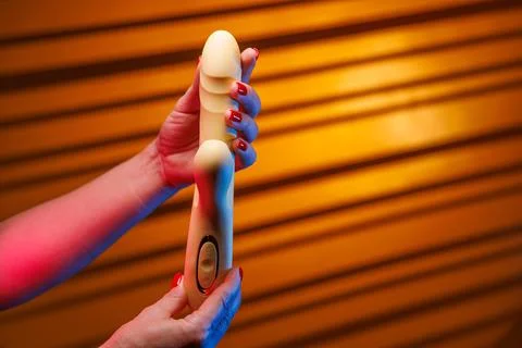 Red nails presenting yellow vibrator in neon glow Stock-Fotos