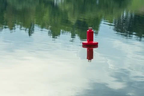 Red navigation buoy floating on the calm water surface of a scenic river wi.. Stock Photos
