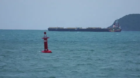 Red navigation sea buoy floating in blue ocean with large cargo ship passing Stock Footage 342916401