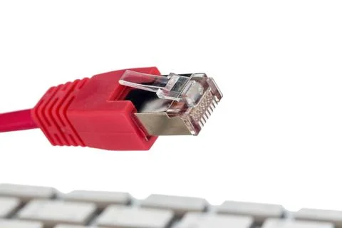 A red network cable of a computer. In the background a computer keyboard statue Foto stock