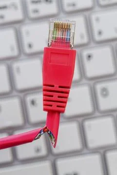 A red network cable of a computer. In the background a computer keyboard statue 写真素材